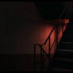 Creepy stairwell in Chaos;Head Noah with red-orange light below and dark shadows above.