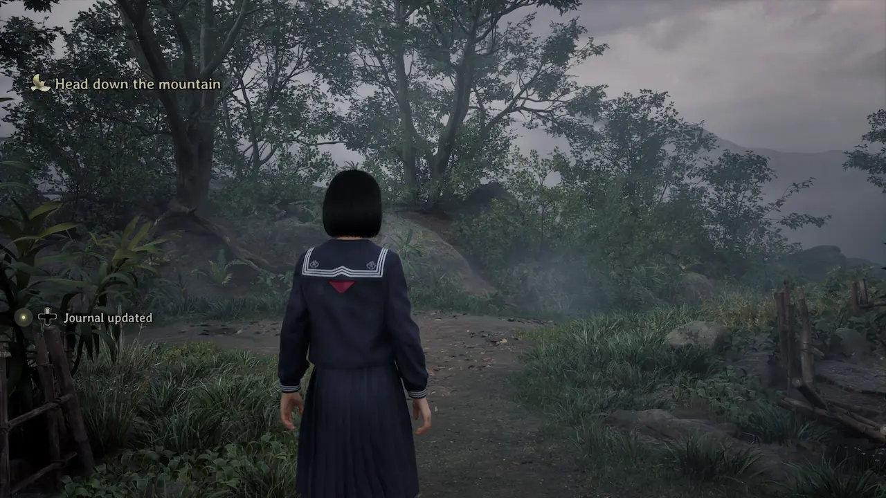Hinako stands on a misty forest path near her home with the “Head down the mountain” objective displayed.