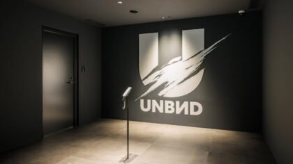 The minimalist entrance lobby of Unbound Games Studio featuring a large white UNBND logo with a brushstroke effect on a dark gray wall.