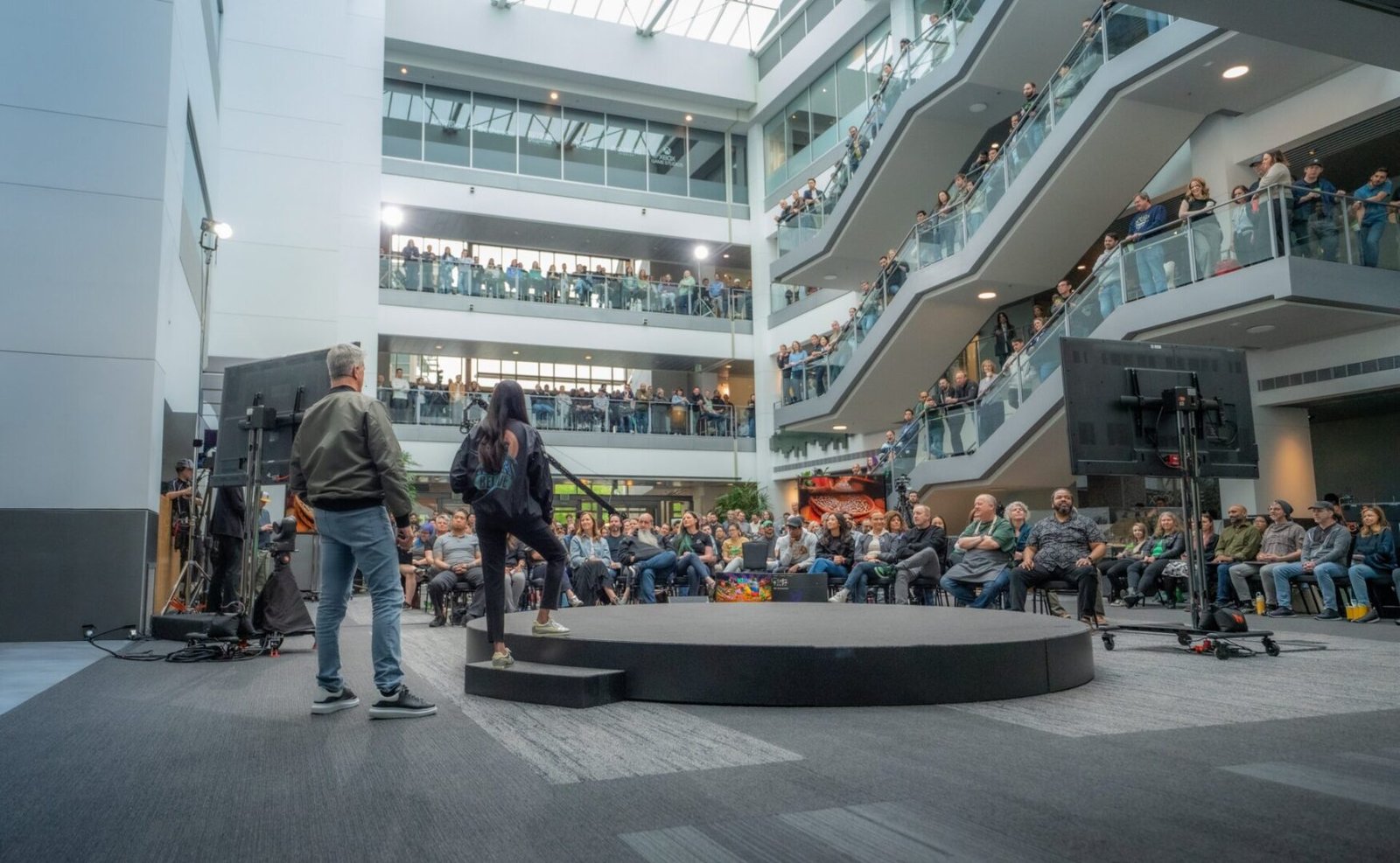 Matt Booty and Asha Sharma addressing a global team of employees during the Xbox brand realignment announcement in a large office atrium.