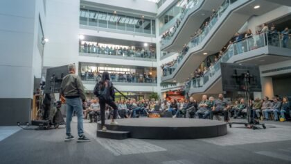 Matt Booty and Asha Sharma addressing a global team of employees during the Xbox brand realignment announcement in a large office atrium.