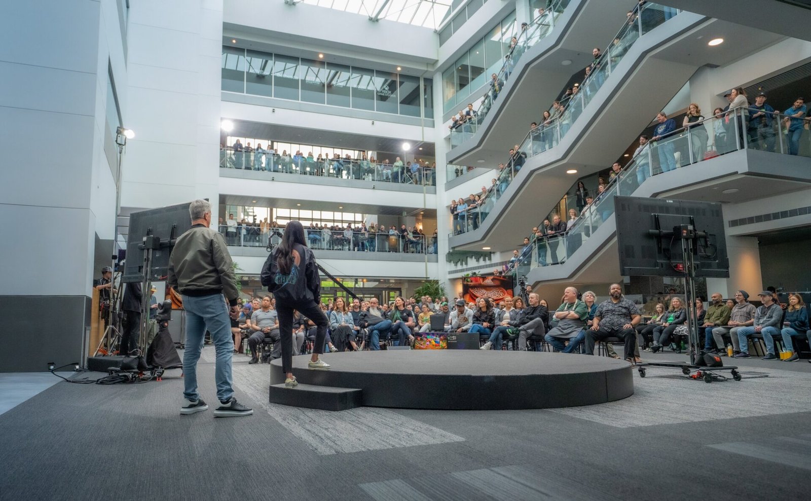 Matt Booty and Asha Sharma addressing a global team of employees during the Xbox brand realignment announcement in a large office atrium.