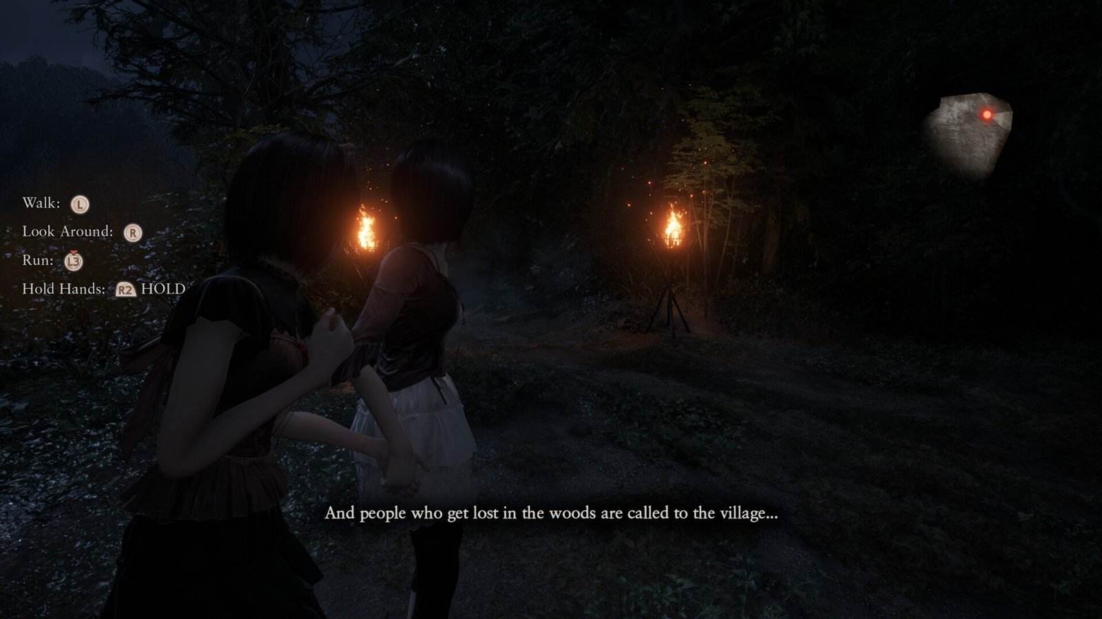 Mio and Mayu holding hands while navigating a dark forest path illuminated by outdoor torches in Fatal Frame 2 Remake.